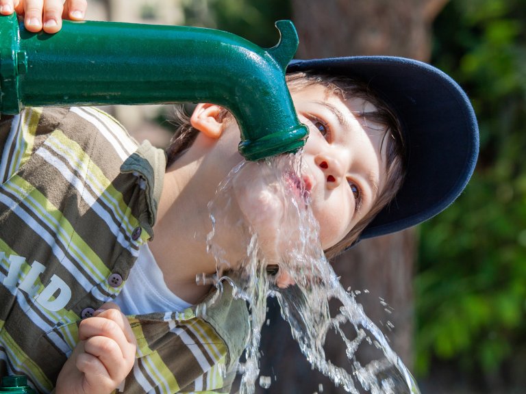 Ein Kind trinkt Wasser direkt aus dem Brunnen.