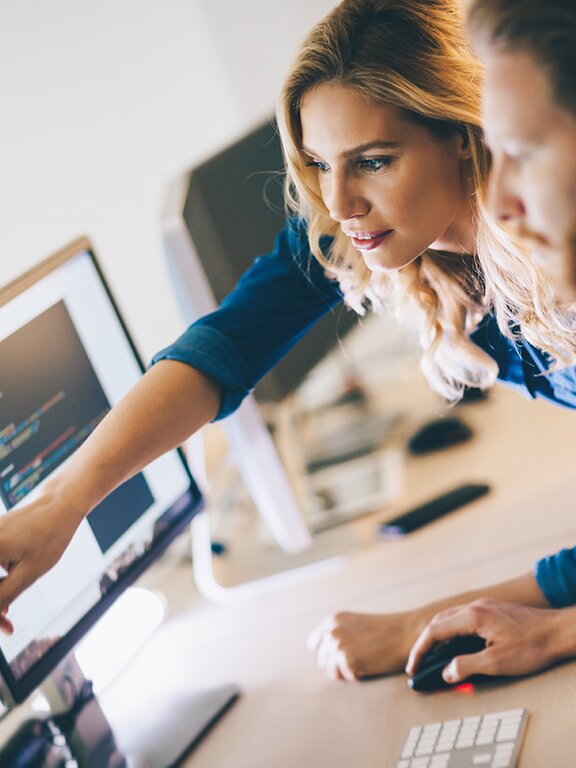 Eine Frau, die einem Kollegen etwas am Computer erklärt. 